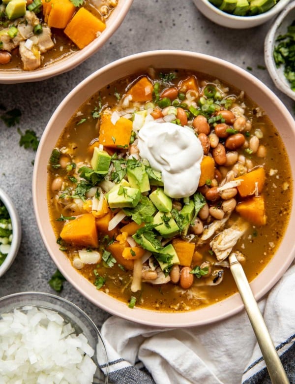 tan bowl of chicken chili soup topped with avocado and sour cream