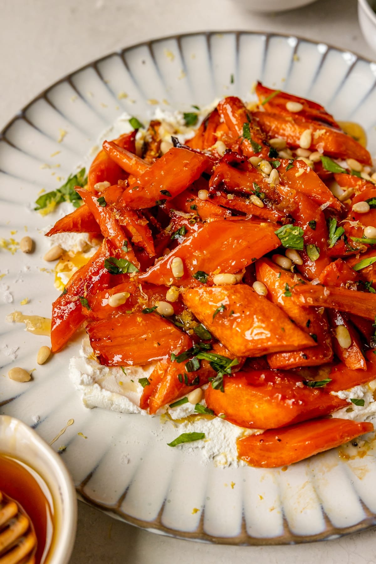 a plate smeared with goat cheese and topped with roasted carrots garnished with lemon zest, parsley, pine nuts and sea salt.